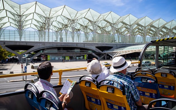 Lisbon bus tour passing by Gare do Oriente with tourists taking photos.