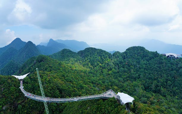 Langkawi Sky Bridge spanning lush green mountains under a cloudy sky.