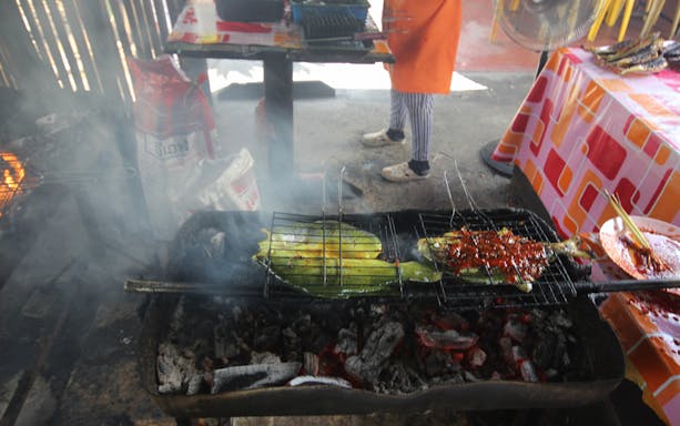 Grilled fish and vegetables on a charcoal grill during Langkawi food tour.