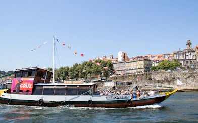 Traditional boat cruising on Douro River with Porto cityscape in the background.