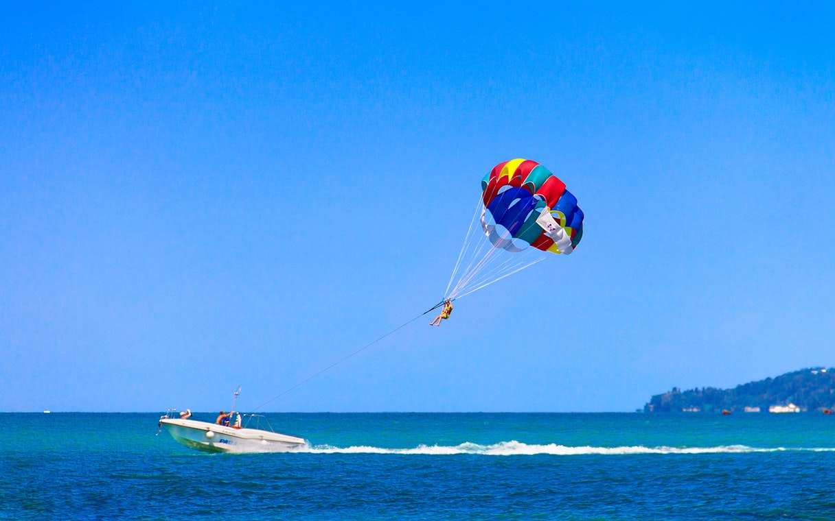 Parasailing over the ocean in Pantai Cenang with a colorful parachute.