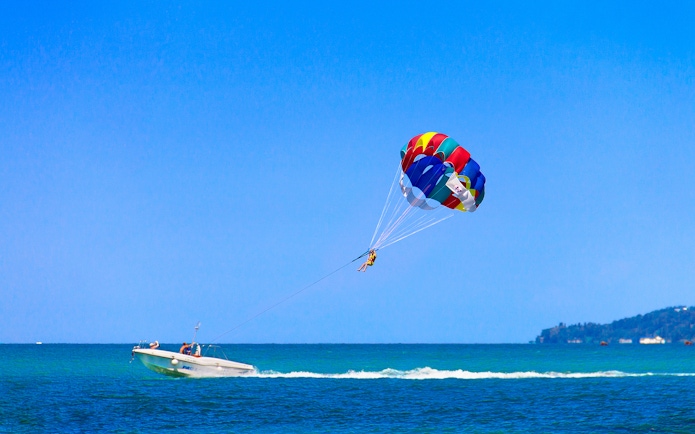 Parasailing over the ocean in Pantai Cenang with a colorful parachute.