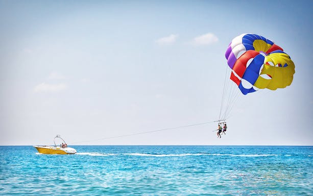 Parasailing over Pantai Cenang beach, Langkawi, with a view of the coastline and ocean.