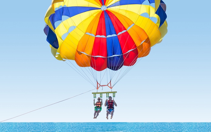 Parasailing over the ocean in Pantai Cenang with colorful parachute.
