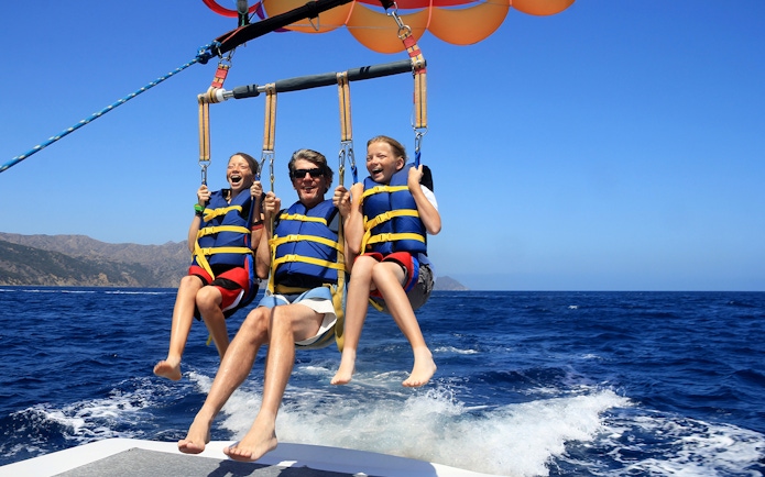 Parasailing over the ocean in Pantai Cenang with two children and an adult.
