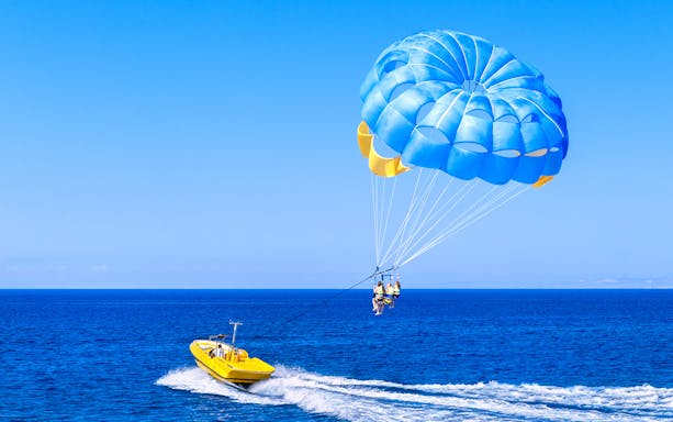 Parasailing over Pantai Cenang beach, Langkawi, with clear blue skies and ocean views.