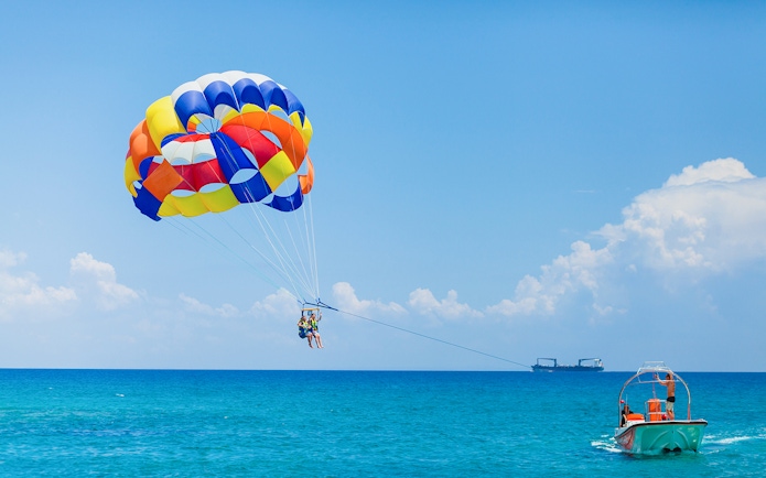 Parasailing over the ocean in Pantai Cenang with colorful parachute and boat.