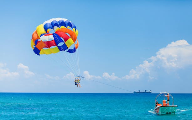 Parasailing over Pantai Cenang beach, Langkawi, with vibrant parachute and scenic ocean view.