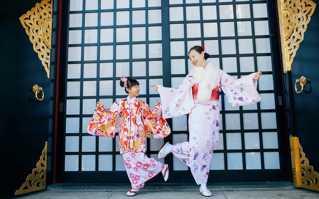 Two people in colorful kimonos dancing in front of a traditional Kyoto gate.