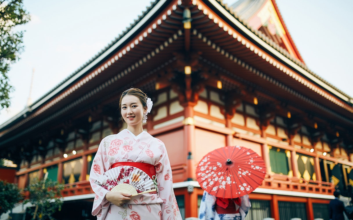 Woman in kimono holding a fan in front of a traditional Kyoto temple.