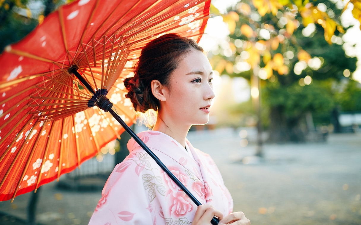Kimono-clad person with red parasol in Kyoto garden.