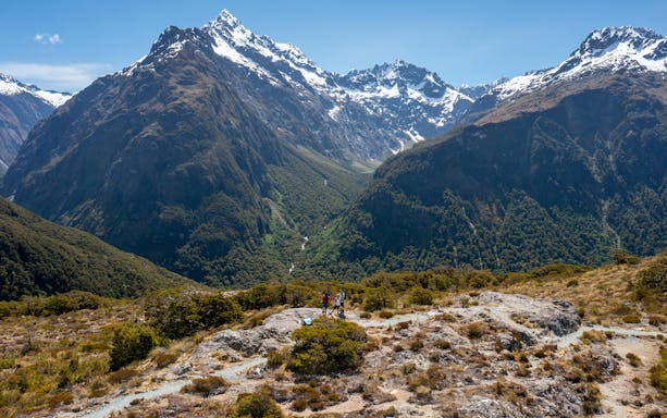 Hikers on Routeburn Track with snow-capped mountains in Fiordland National Park.