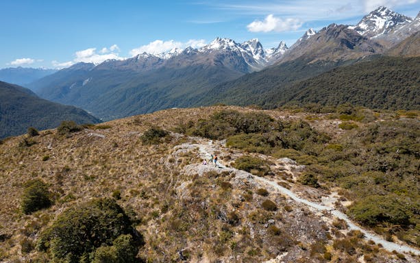 Hikers on Routeburn Track with snow-capped mountains in Fiordland National Park.