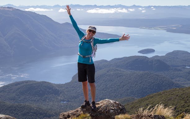 Hiker on Kepler Track summit with Lake Te Anau view during guided heli hike.