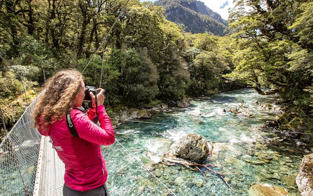 Person photographing a river on a suspension bridge during a Lake Marian hiking tour.