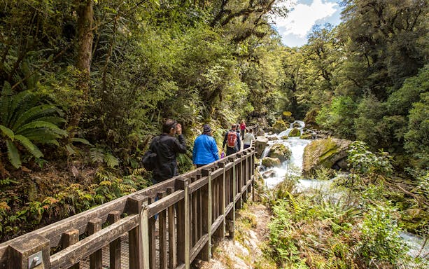 Hikers on a wooden path through lush forest near a waterfall on Lake Marian trail.