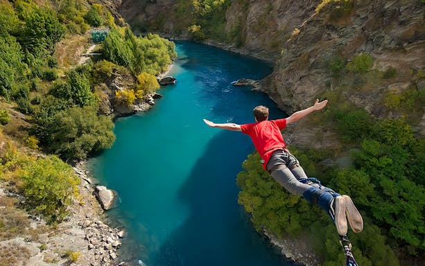 Person bungee jumping over Kawarau River in Arrowtown, New Zealand, surrounded by lush greenery.