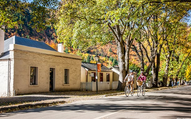 Cyclists riding through tree-lined street in Arrowtown, New Zealand.