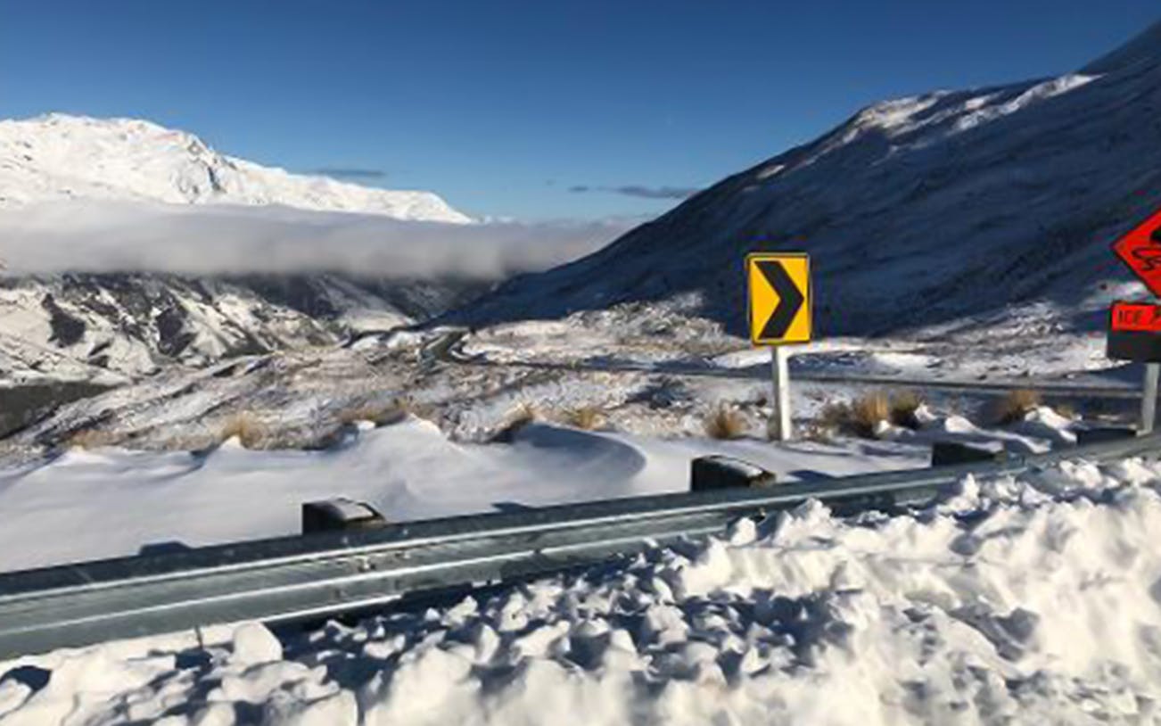 Snow-covered mountain road with caution signs in Arrowtown, New Zealand.