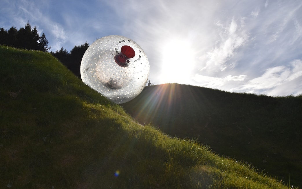 Zorb ball rolling down a grassy hill under a bright sky.