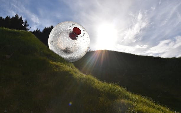 Zorb ball rolling down a grassy hill under a bright sky.