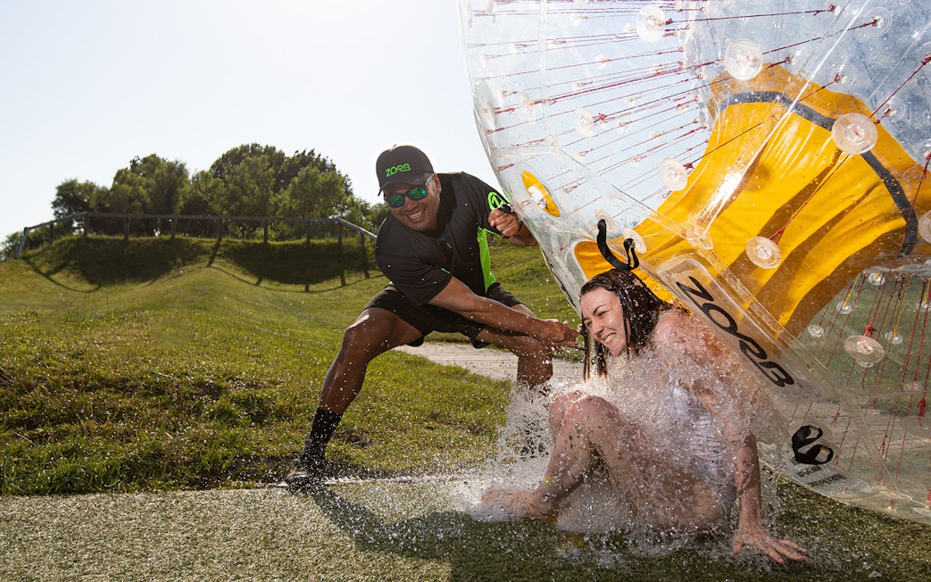Person exiting a Zorb giant inflatable ball ride on a grassy hill.