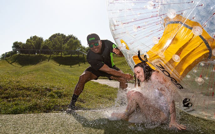 Person exiting a Zorb giant inflatable ball ride on a grassy hill.