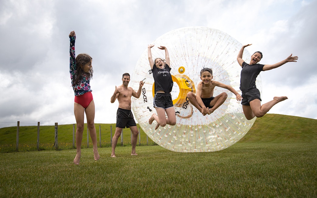 Group enjoying Zorb giant inflatable ball ride on grassy hill.