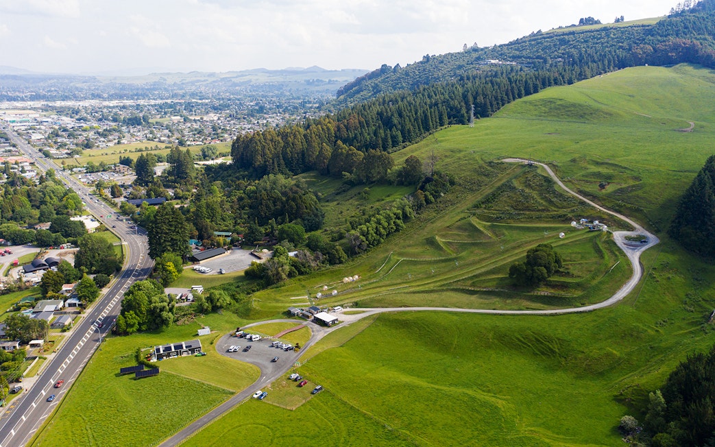 Aerial view of Zorb giant inflatable ball ride location in lush green hills near a city.