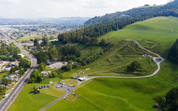 Aerial view of Zorb giant inflatable ball ride location in lush green hills near a city.