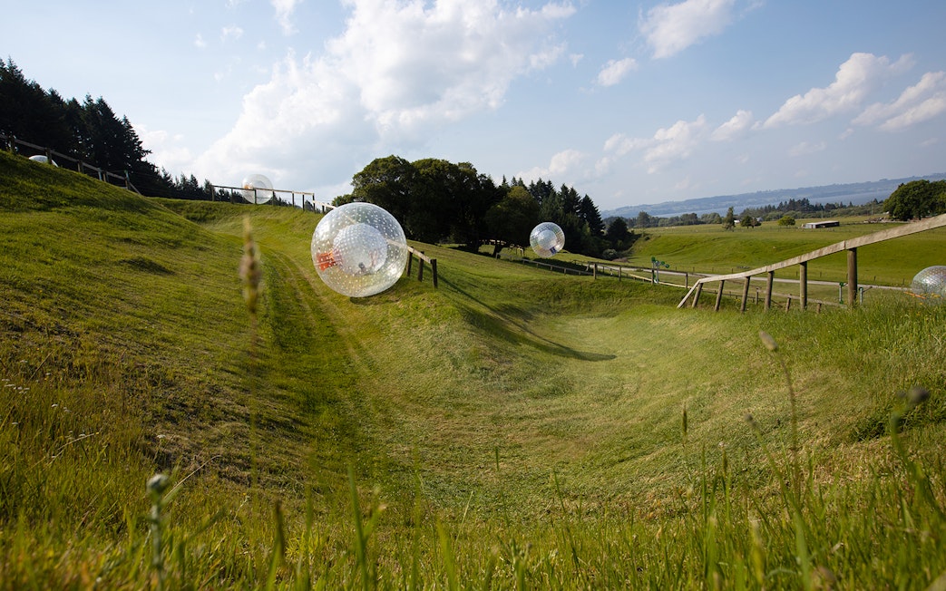 Zorb balls rolling down a grassy hill in a countryside setting.