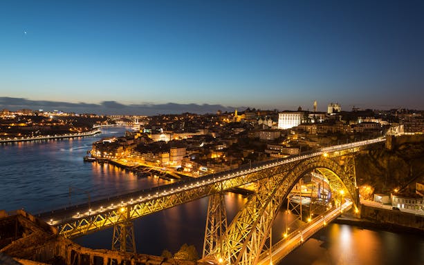 Porto cityscape at night with Dom Luís I Bridge illuminated over Douro River.