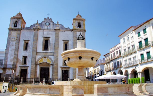Central square in Évora with a historic church and fountain, part of the Wine Tour from Lisbon.