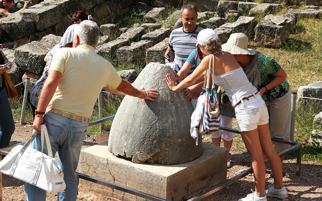 Guests touching the Sacred Omphalos stone in Delphi, Greece.
