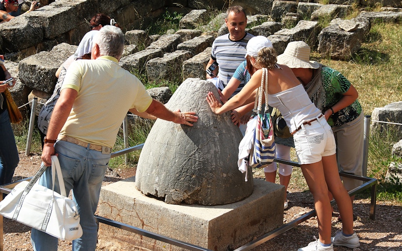 Guests touching the Sacred Omphalos stone in Delphi, Greece.