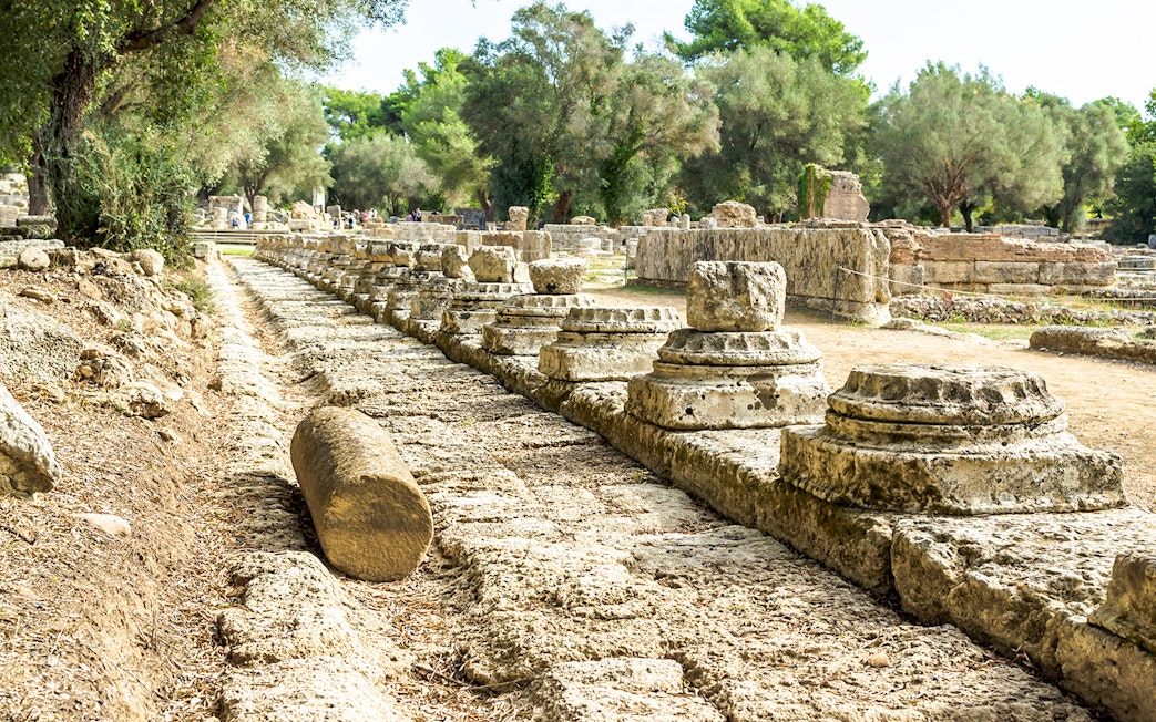Ancient ruins of Olympia with stone columns and trees in Greece.