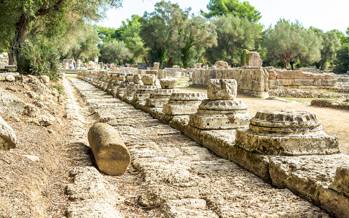 Ancient ruins of Olympia with stone columns and trees in Greece.