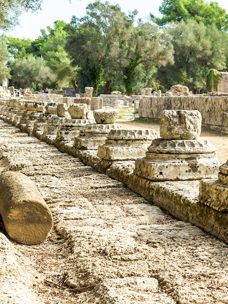 Ancient ruins of Olympia with stone columns and trees in Greece.