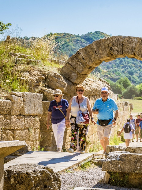 Visitors walking through ancient stone archway at Olympia archaeological site.