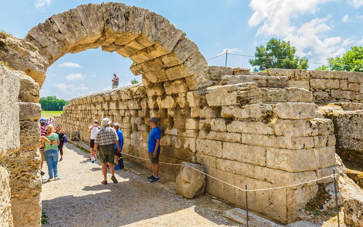 Visitors exploring the ancient stone archway at Olympia Archaeological Site, Greece.