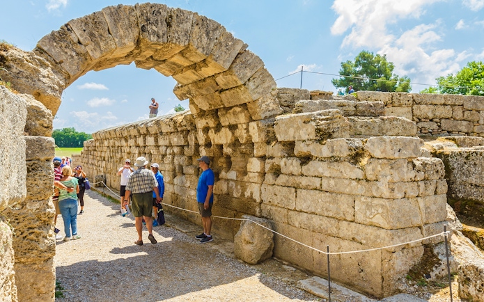 Visitors exploring the ancient stone archway at Olympia Archaeological Site, Greece.