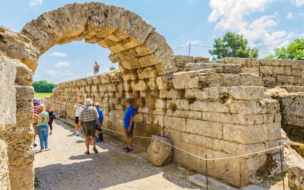Visitors exploring the ancient stone archway at Olympia Archaeological Site, Greece.