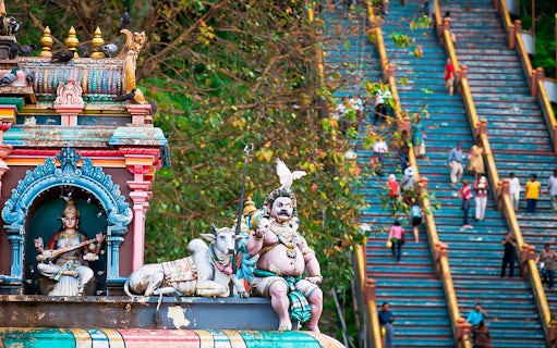 Batu Caves colorful temple statues with visitors climbing stairs in Kuala Lumpur.