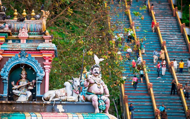 Batu Caves colorful temple statues with visitors climbing stairs in Kuala Lumpur.