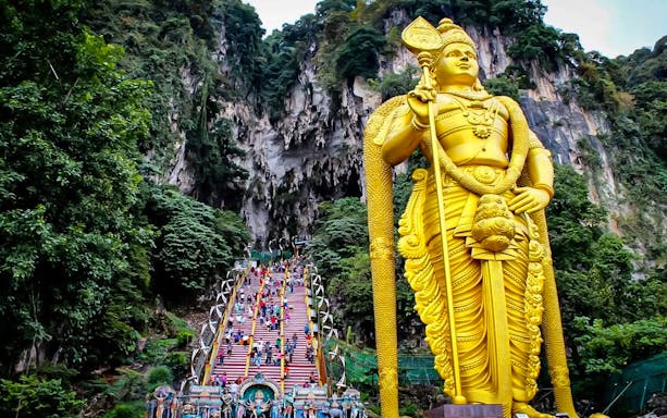 Batu Caves entrance with golden statue and colorful steps, Kuala Lumpur tour.