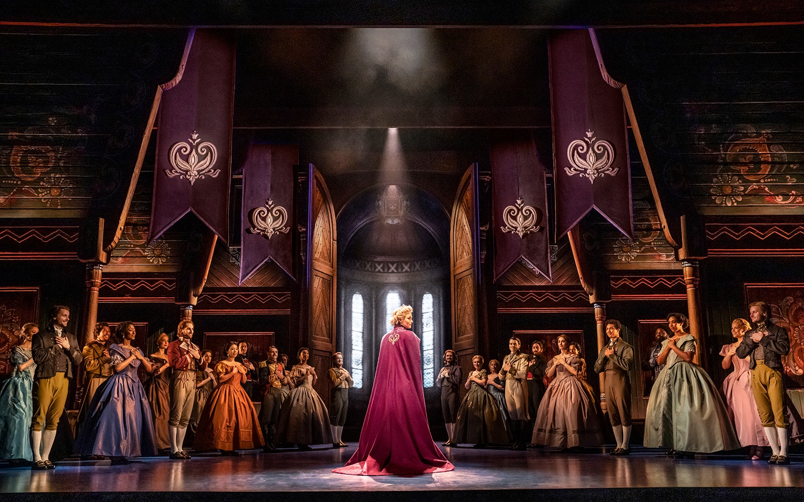 Cast of Frozen The Musical performing on stage with ornate banners and costumes.
