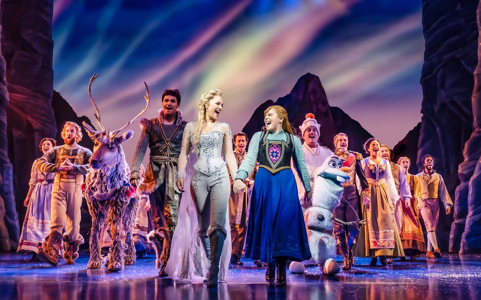 Cast performing on stage in Frozen The Musical with colorful backdrop.