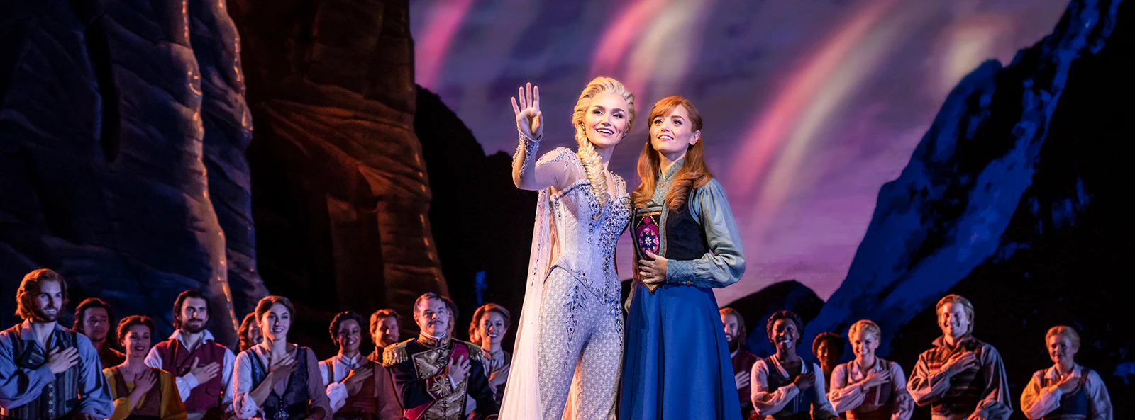 Performers on stage during Frozen The Musical with a mountain backdrop.