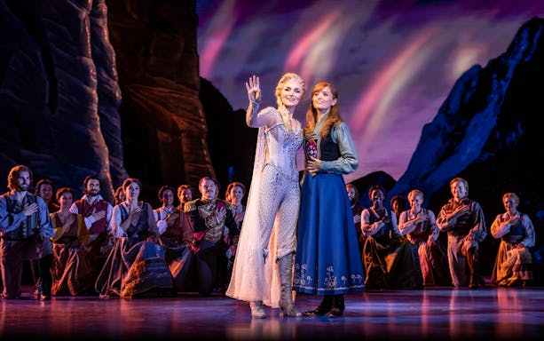Performers on stage during Frozen The Musical with a mountain backdrop.