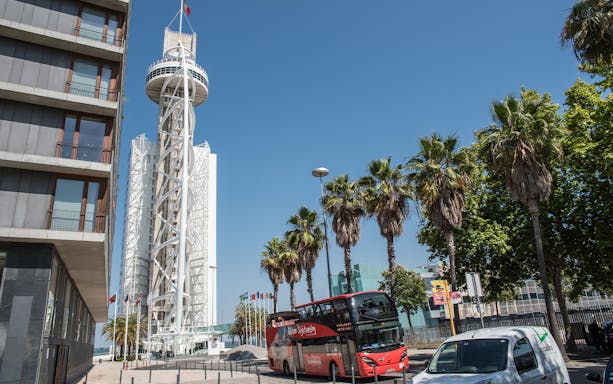 Lisbon hop-on hop-off bus near Vasco da Gama Tower with palm trees.